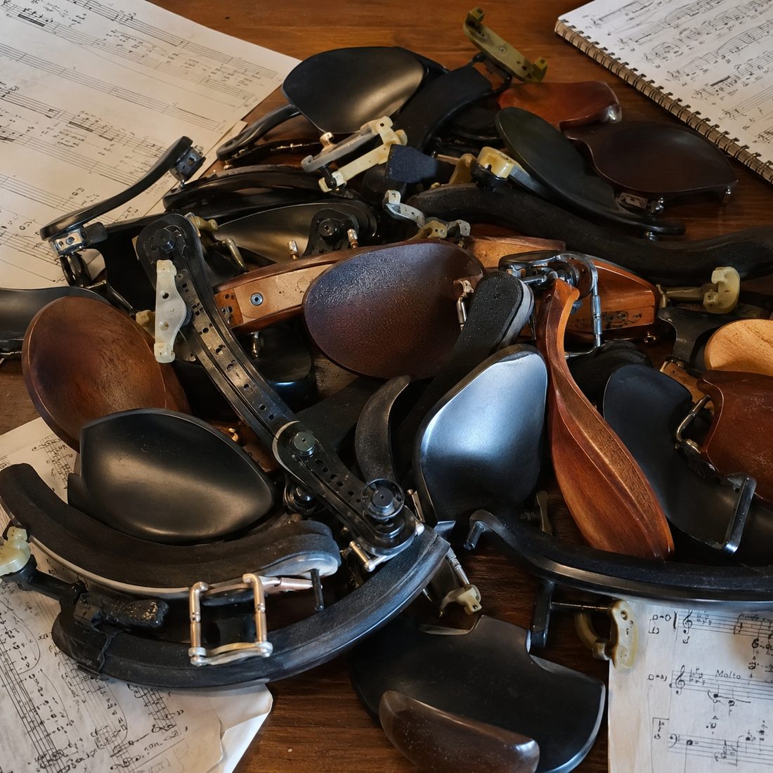 A pile of discarded shoulder rests and chin rests on a table covered in sheet music